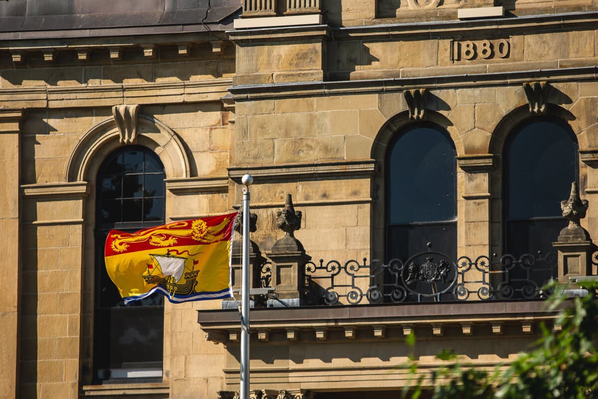 The New Brunswick flag flies in front of the provincial legislative assembly building in Fredericton on July 26, 2025. (The Canadian Press/Giordano Ciampini)