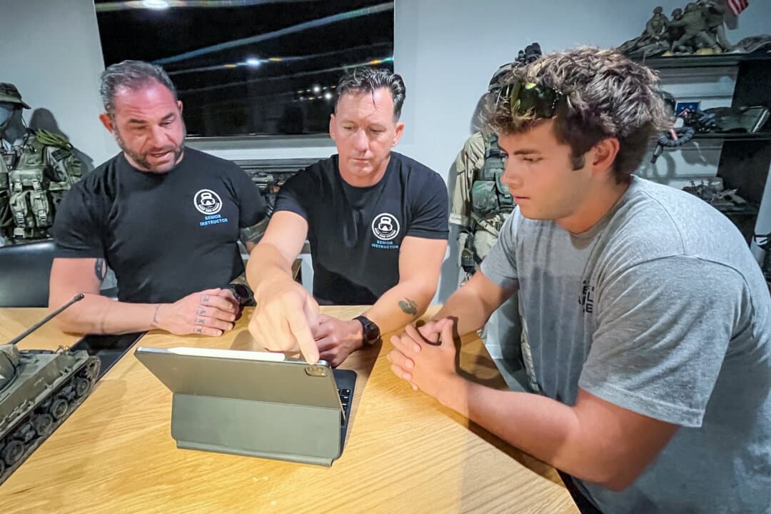 Lysander Caligo (L) and Travis Haley (C), both senior instructors at Deep End Fitness Scottsdale, and military-bound trainee Connor Schutza review a daily lesson, in Scottsdale, Ariz., on May 21, 2026. (Allan Stein/The Epoch Times)