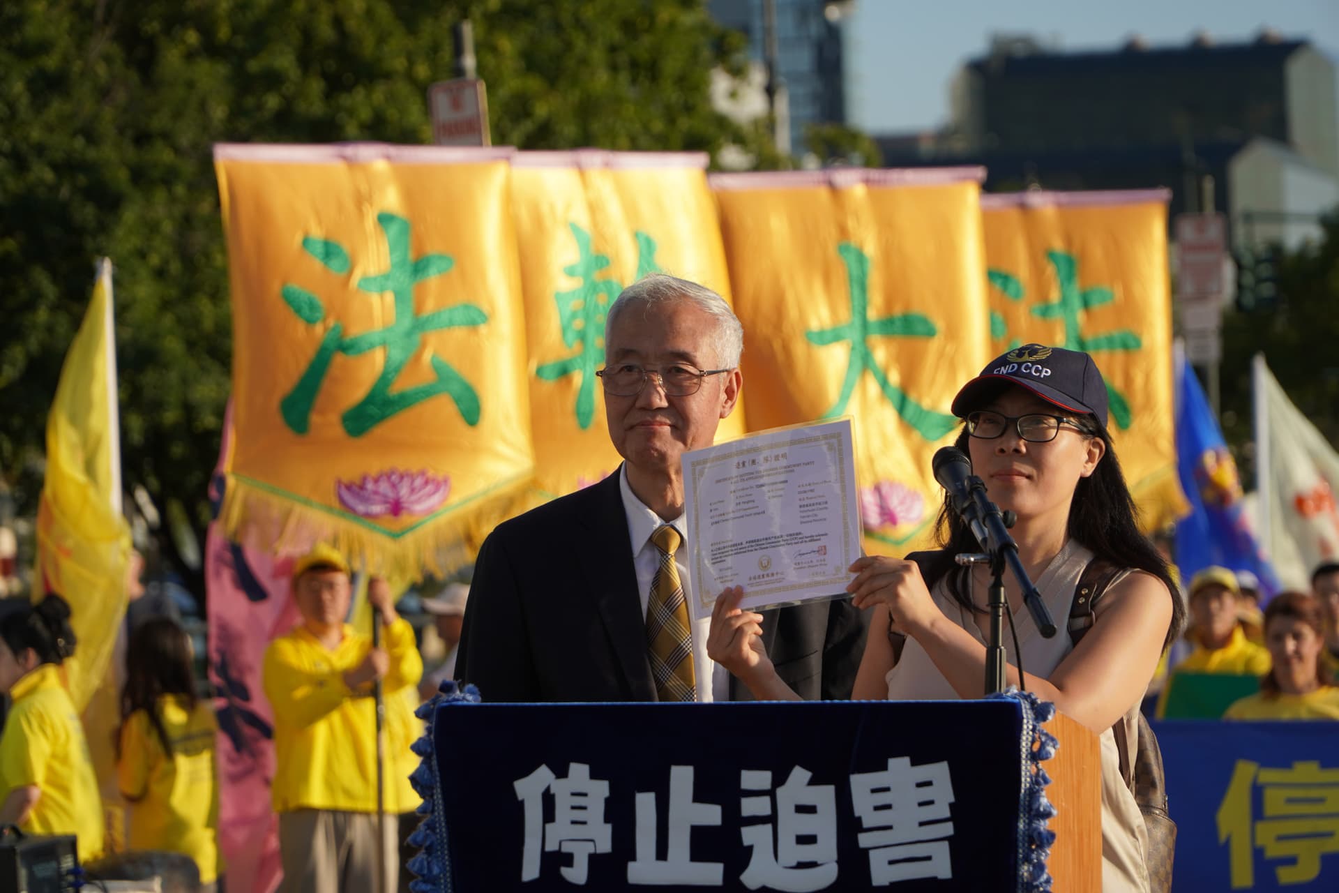 Hao Fangfang (R) holds up her certificate declaring her decision to quit the Chinese Communist Party and its affiliated organizations, while Wang Zhiyuan (L), chairman of the Global Service Center for Quitting the CCP, looks on, in New York City on July 20, 2026. (Nicholas Zifcak/The Epoch Times)