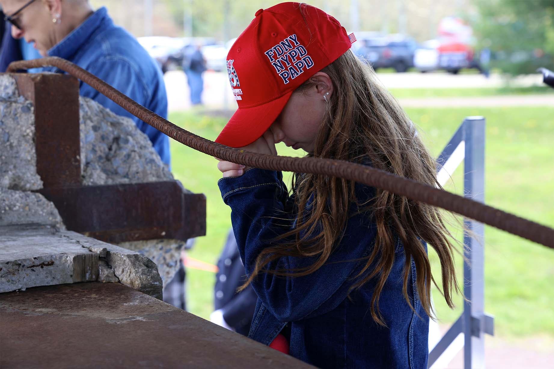 A young girl says a prayer next to the I-beam on display during the Steel Across America tour. (Tunnel to Towers)