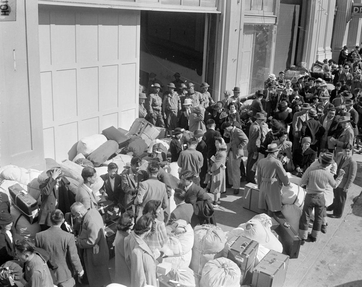 As military police stand guard, people of Japanese descent wait at a transport center for relocation to an internment center, in San Francisco on April 6, 1942. (AP Photo)