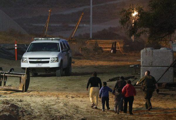 A U.S. Border Patrol agent escorts migrants detained for climbing over the border wall from Playas de Tijuana, Mexico, to San Ysidro, Calif., on Dec. 3, 2018. (Rebecca Blackwell/AP Photo)