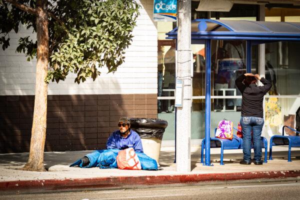 A homeless man sits on the sidewalk at a bus station in Costa Mesa, Calif., on Oct. 26, 2020. (John Fredricks/The Epoch Times)