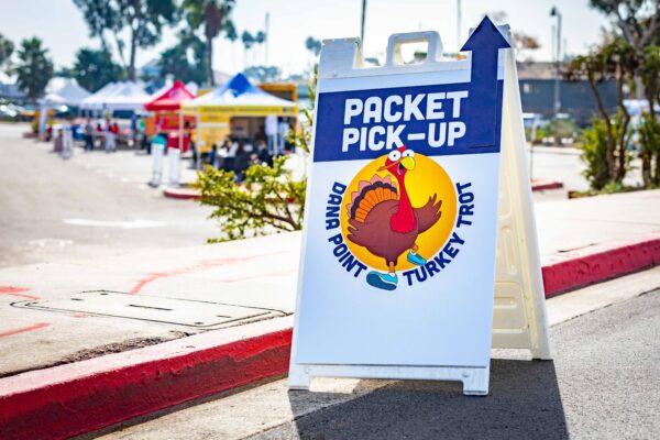 A sign directs participants in the annual Turkey Trot to pick up their runner packets at a drive-thru location in Dana Point, Calif., on Nov. 21, 2020. (John Fredricks/The Epoch Times)