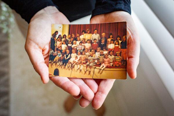 Elizabeth Sitton holds a photo of herself surrounded by other children her age part of the Fellowship commune, in her home in Culver City, Calif., on Dec. 8, 2020. (John Fredricks/The Epoch Times)