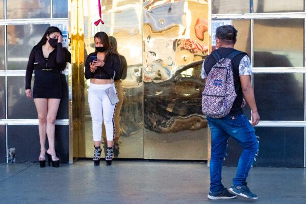 A man walks by two women standing near a strip club in Zona Norte, Tijuana, Mexico, on Jan. 16, 2021. (John Fredricks/The Epoch Times)