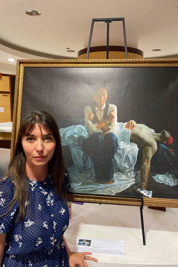 Johanna Schwaiger stands next to the painting “A Tragedy in China” at "The Art of Zhen Shan Ren" exhibit in Fullerton, Calif., on Feb. 25, 2021. (Jack Bradley/The Epoch Times)