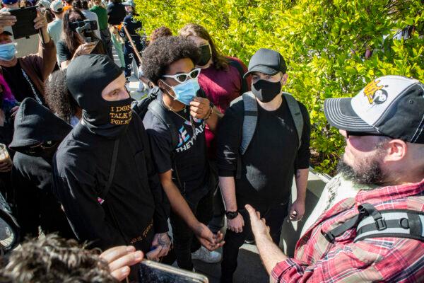 Men dressed in black block a counter-protestor holding a sign saying "WE LIKE DAVE" (Chappelle) as protestors and counter-protestors voicing for or against a popular Dave Chappelle comedy special currently airing on Netflix gather in front of Netflix's Vine Street offices in Los Angeles on Oct. 20, 2021. (John Fredricks/The Epoch Times)