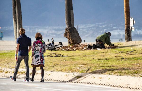 People walk past a homeless man in Venice Beach, Calif., on Jan. 27, 2021. (John Fredricks/The Epoch Times)