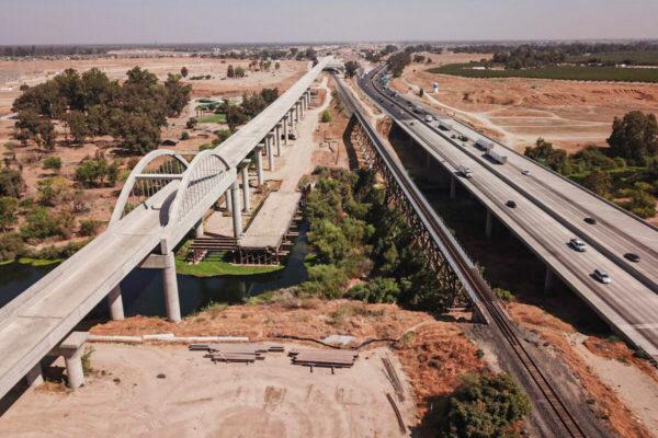In this aerial image, vehicles drive past farmland and part of the California High Speed Rail Authority San Joaquin River viaduct construction project alongside US Highway 99 through the Central Valley between Madera County and Fresno County, Calif., on Aug. 26, 2021. (Patrick T. Fallon/AFP via Getty Images)