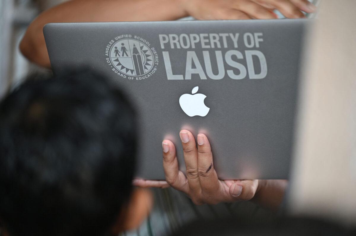 A school administrator confirms student health check data on a laptop computer as students and parents wait in line to enter school at Grant Elementary School in Los Angeles on Aug. 16, 2021. (Robyn Beck/AFP via Getty Images)