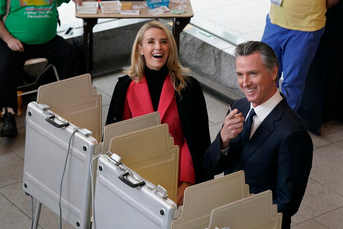 California Gov. Gavin Newsom and his wife Jennifer Siebel Newsom laugh as they pause from voting and spot photographers above, at a voting center in Sacramento on Nov. 8, 2022. (Rich Pedroncelli/AP Photo)