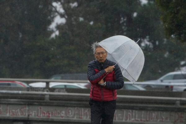 A man uses an umbrella to shield from the wind and rain in Oakland, Calif., on March 21, 2023. (AP Photo/Godofredo A. Vásquez)
