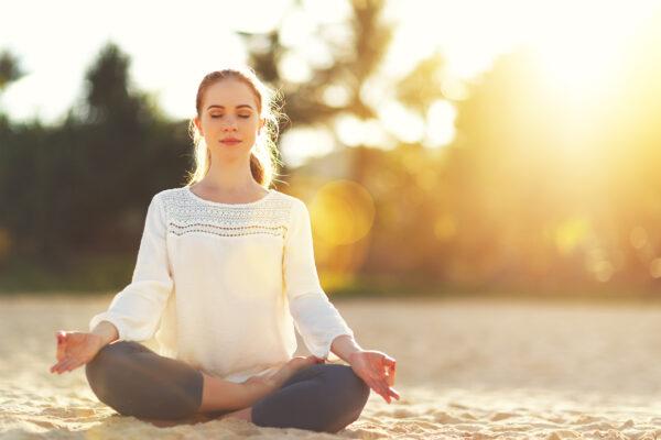 A woman practices yoga and meditates in the lotus position on the beach. (Shutterstock)