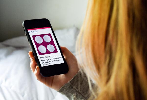 A woman looks at an abortion pill—mifepristone—displayed on a smartphone in Arlington, Va., on May 8, 2020. (Olivier Douliery/AFP via Getty Images)