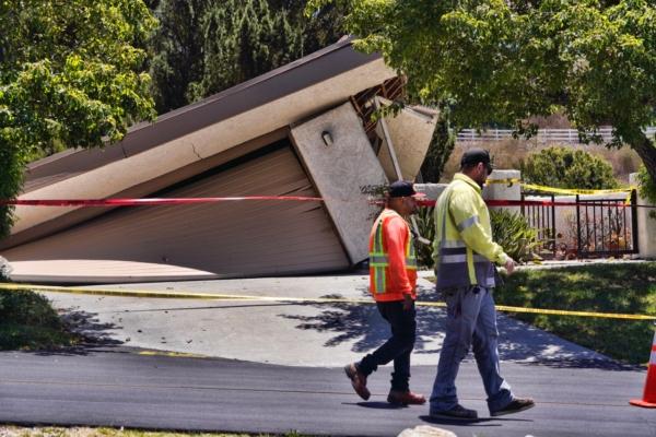 City employees pass a damaged house teetering over a ravine in Rolling Hills Estates on the Palos Verdes Peninsula in Los Angeles County on July 10, 2023. (Richard Vogel/AP Photo)
