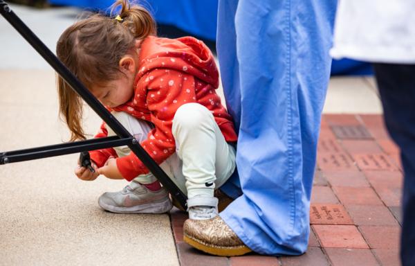 A child plays with a news tripod between the legs of her mother in Orange, Calif., on June 3, 2022. (John Fredricks/The Epoch Times)