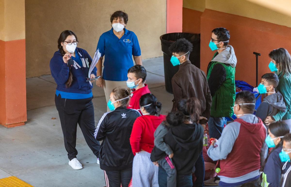 Migrants listen to pre-recorded instructions in Spanish before entering their hotel as Gloria Gomez (top right) gives further instructions in Indio, Calif., on Oct. 18, 2021. (John Fredricks/The Epoch Times)
