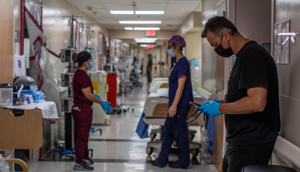 The medical director of the Intensive Care Unit (ICU) answers text messages on his phone while nurses stand outside patients' bedrooms at Providence Cedars-Sinai Tarzana Medical Center in Tarzana, Calif., on Jan. 3, 2021. (Apu Gomes/AFP via Getty Images)