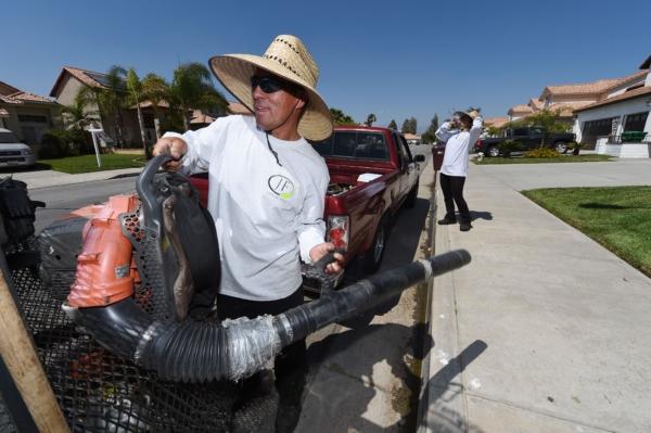 A worker (L) grabs a leaf blower as his co-worker takes a drink of water, while doing landscape work, in Perris, Calif., on June 16, 2016. (Robyn Beck/AFP via Getty Images)