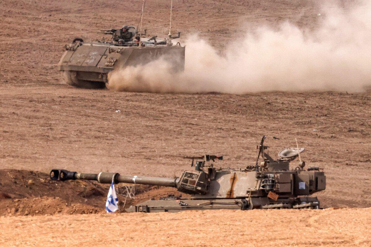 An Israeli army armoured tracked vehicle moves near a stationed artillery howitzer at a position along the border with the Gaza Strip in southern Israel, on Oct. 31, 2023. (Jack Guez/AFP via Getty Images)