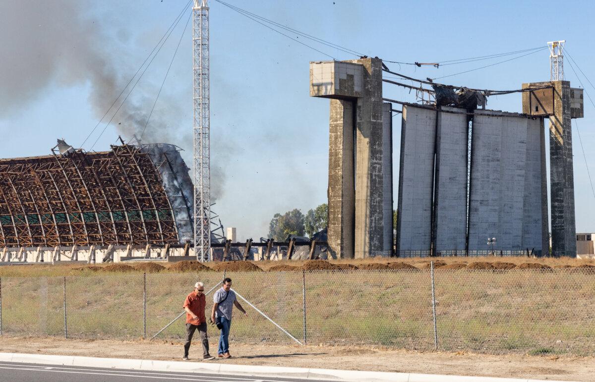 Men walk as a fire continues to burn a historic blimp hangar in Tustin, Calif., on Nov. 14, 2023. (John Fredricks/The Epoch Times)