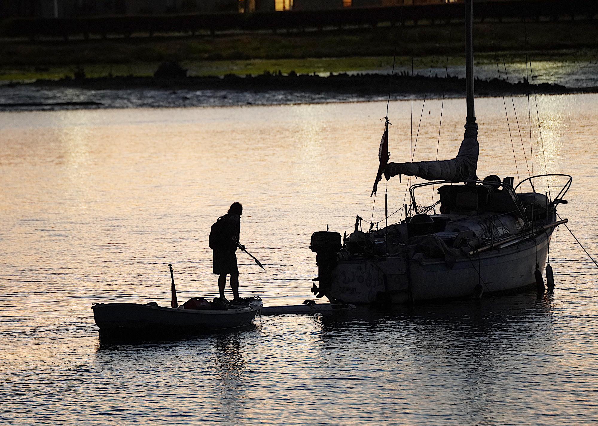 A homeless man brings his small boat alongside a derelict vessel anchored illegally in the Oakland Estuary on Nov. 13, 2023. (Allan Stein/The Epoch Times)