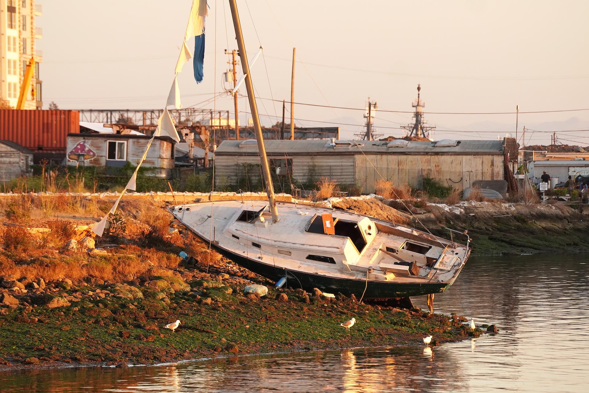 An abandoned, derelict sailboat lies stranded along the shoreline of the Oakland Estuary on Nov. 13, 2023. (Allan Stein/The Epoch Times)