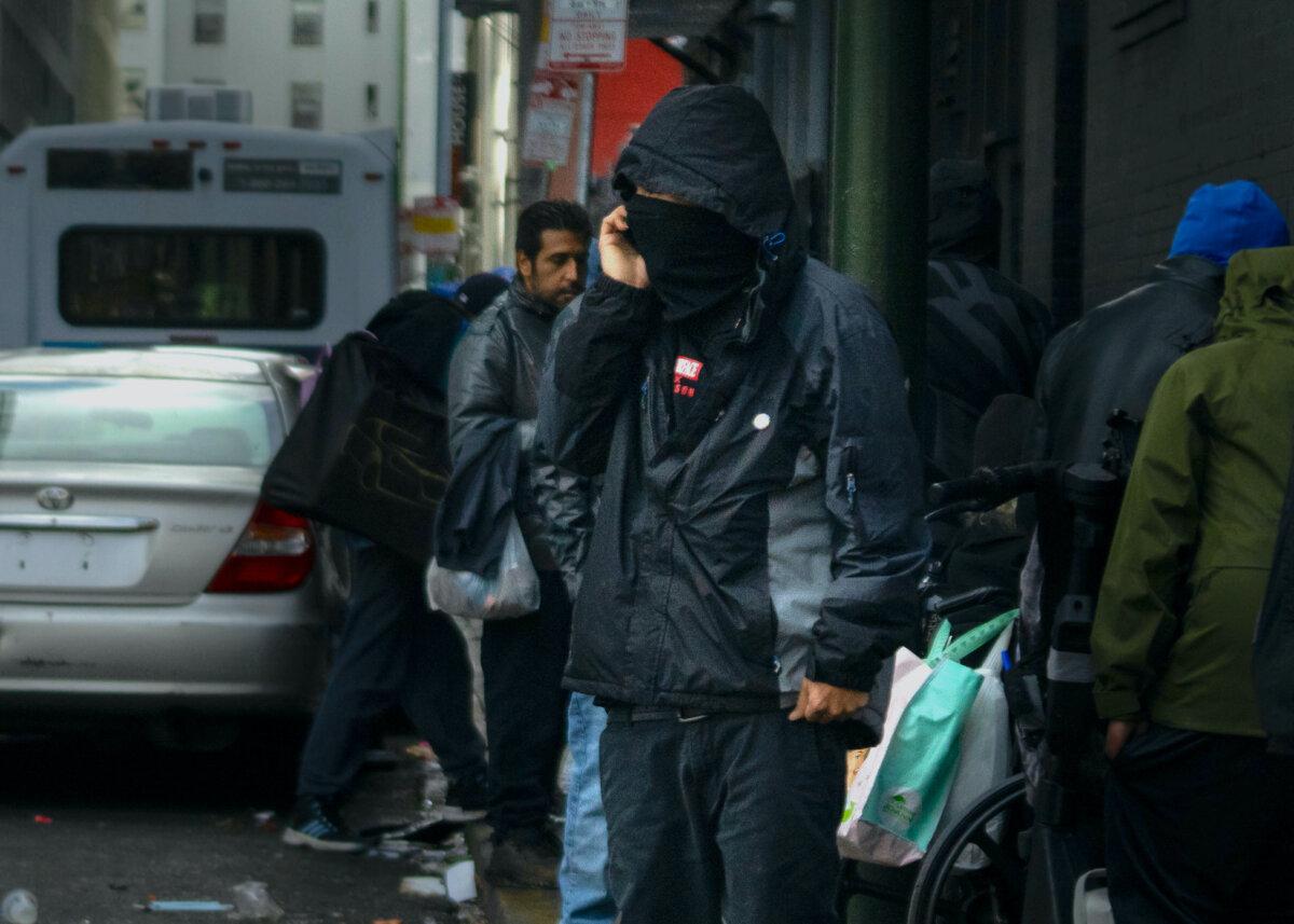 An alleged drug dealer stands near a row of drug addicts in San Francisco, Calif., on Feb. 23, 2023. (John Fredricks/The Epoch Times)