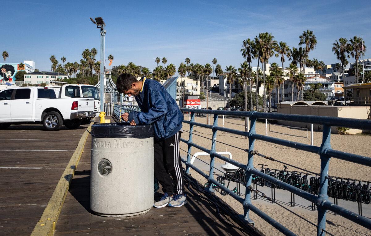 A homeless man looks for food in a trash can in Santa Monica, Calif., on Dec. 8, 2023. (John Fredricks/The Epoch Times)