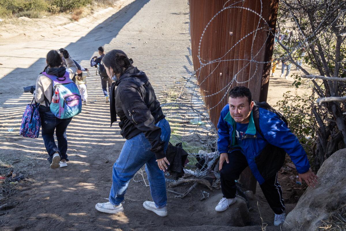 Illegal immigrants pass through a gap in the U.S. border wall to await processing by Border Patrol agents in Jacumba, Calif., on Dec. 7, 2023. (John Fredricks/The Epoch Times)