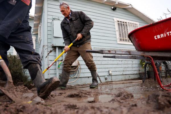 Family members clean mud from a home damaged by flooding, with the floodwater line visible on the house, the day after an explosive rainstorm deluged areas in San Diego on Jan. 23, 2024. The intense rains forced dozens of rescues while flooding roadways and homes and knocking out electricity for thousands of residents. (Mario Tama/Getty Images)