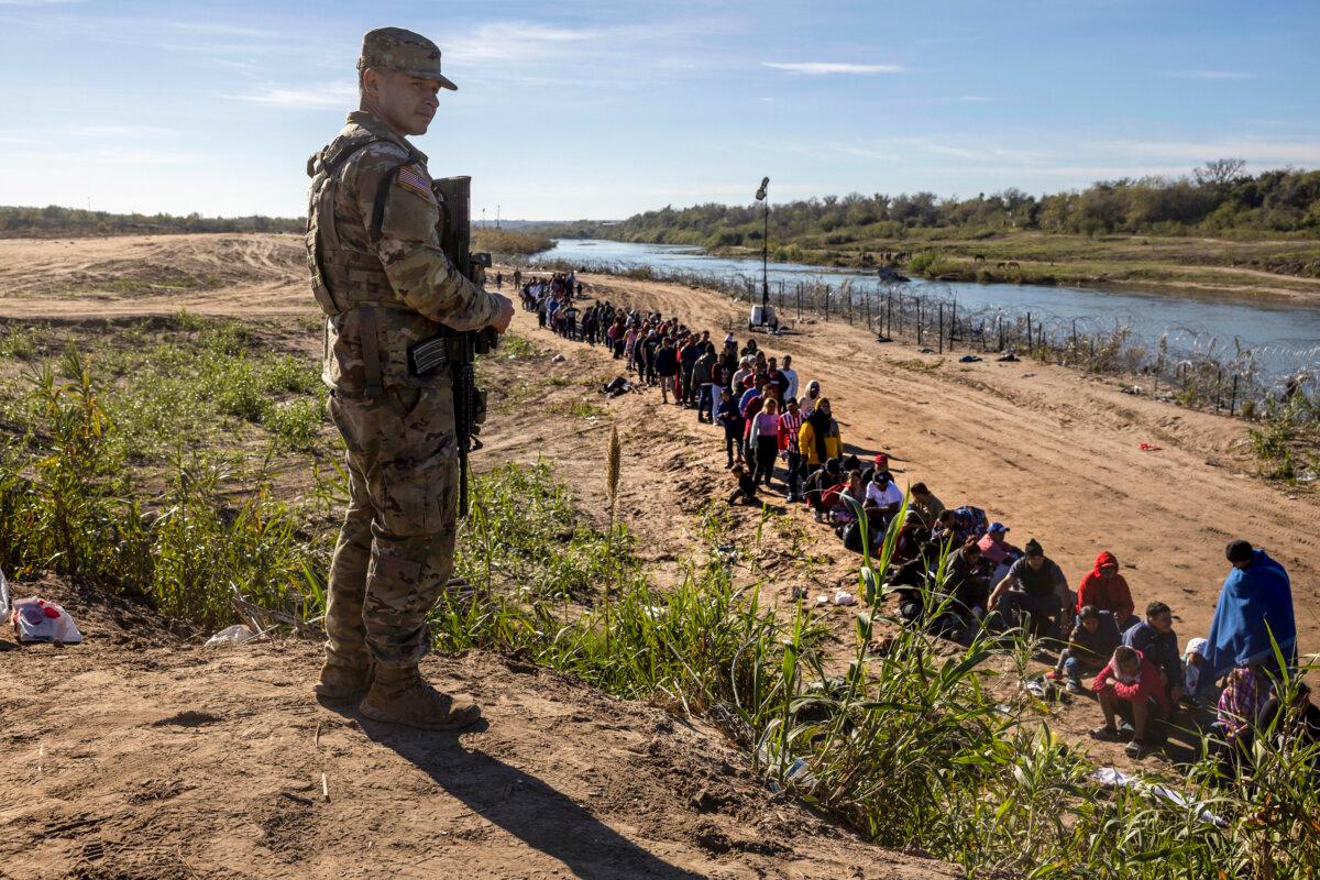 A Texas National Guard soldier watches over a group of more than 1,000 migrants who had crossed the Rio Grande from Mexico in Eagle Pass, Texas, on Dec. 18, 2023. (John Moore/Getty Images)