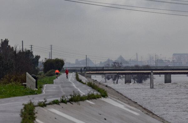 Runners jog along the Los Angeles River during a rainstorm in Long Beach, Calif., on Feb. 6, 2024. (John Fredricks/The Epoch Times)