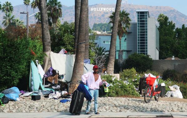 A man stands in front of a homeless encampment, with the Hollywood sign in the background, in Los Angeles on Sept. 23, 2019. (Mario Tama/Getty Images)