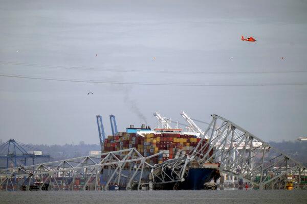 A helicopter flies over a container ship as it rests against wreckage of the Francis Scott Key Bridge, as seen from Pasadena, Md., on Tuesday, March 26, 2024. (Mark Schiefelbein/AP Photo)