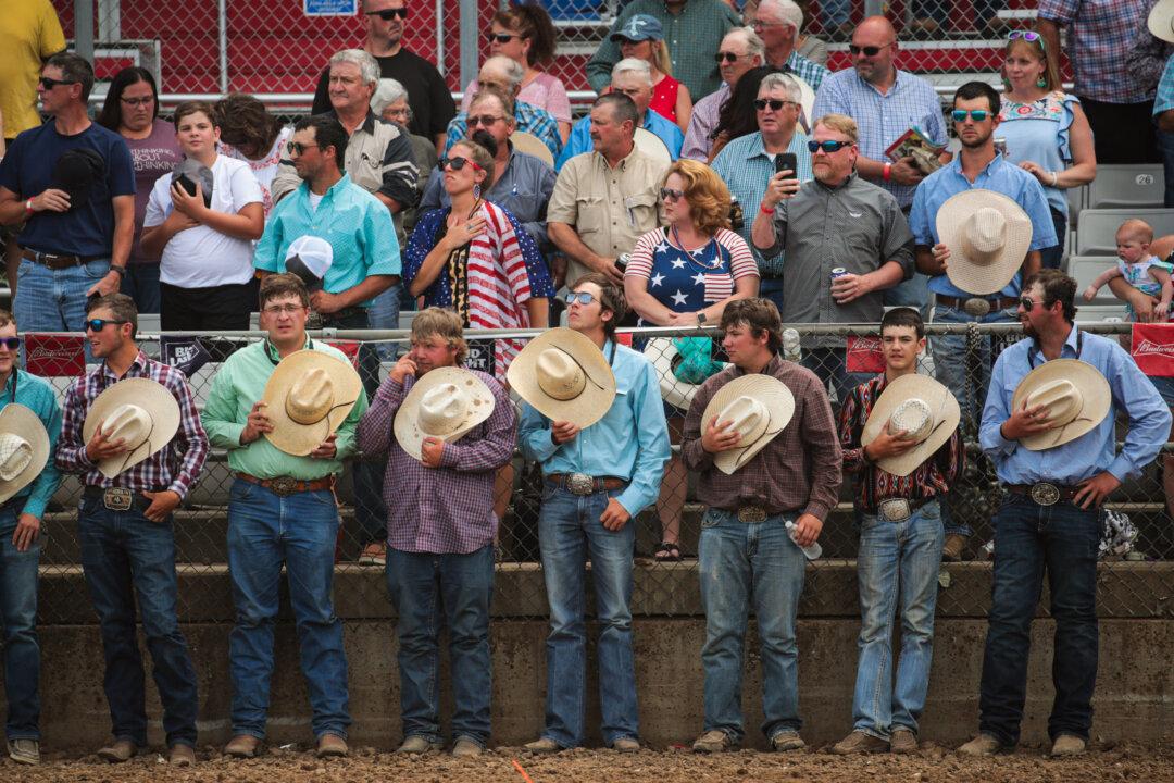 (Top) A parachutist brings in the U.S. flag before the start of the 101st annual Black Hills Roundup rodeo in Belle Fourche, S.D., on July 4, 2020. The town celebrated Independence Day with the rodeo, a parade, a street dance, and a carnival. (Bottom) Guests remove their hats during a salute to veterans before the start of the rodeo. (Scott Olson/Getty Images)