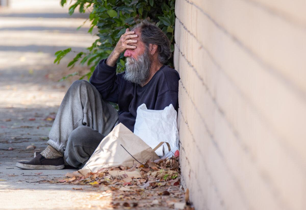 A homeless man sits near a busy street in Santa Ana, Calif., on July 15, 2024. (John Fredricks/The Epoch Times)