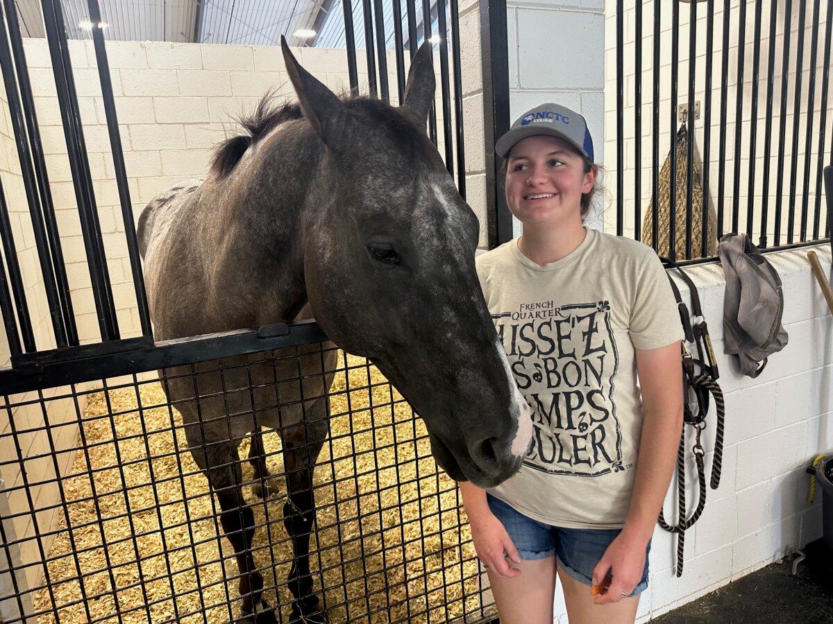 Hurricane Helene evacuee Maggie Nelson chats with visitors next to her horse, Trapper, outside a stall at the World Equestrian Center in Ocala, Fla., on Sept. 27, 2024. (Nanette Holt/The Epoch Times)
