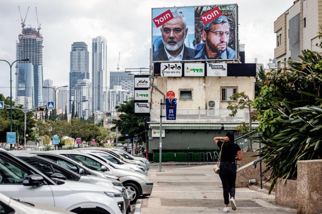 A woman walks near a billboard displaying portraits of Hamas leader Mohammed Deif (R) and Ismail Haniyeh with the slogan “assassinated” written in Hebrew, in Tel Aviv, Israel, on Aug. 2, 2024. (Oren Ziv/AFP via Getty Images)
