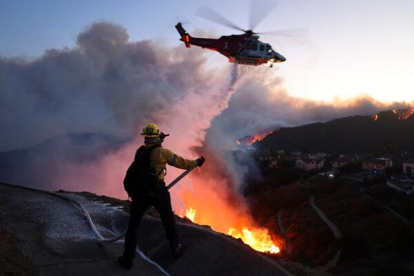 Fire personnel respond to homes destroyed while a helicopter drops water as the Palisades Fire grows in Pacific Palisades, California on January 7, 2025. (David Swanson / AFP via Getty Images)