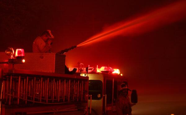 A firefighter wipes his eyes as he sprays water on a burning home while battling the Eaton Fire in Altadena, Calif., on Jan. 8, 2025. (Justin Sullivan/Getty Images)