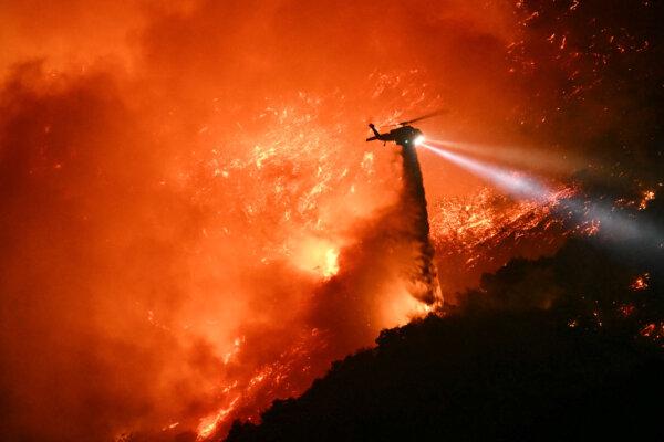 A fire fighting helicopter drops water as the Palisades fire grows near the Mandeville Canyon neighborhood and Encino, Calif., on Jan. 11, 2025. (Patrick T. Fallon/AFP via Getty Images)