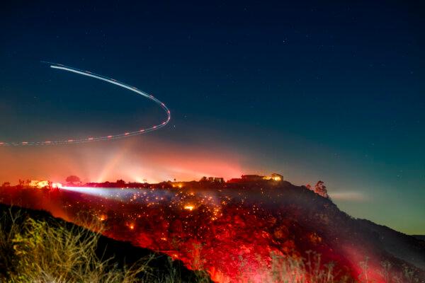 In this long exposure photo, a helicopter surveys the scene during the Lilac fire in unincorporated San Diego County, California on Jan. 21, 2025. (Photo by Josh Edelson / AFP via Getty Images)