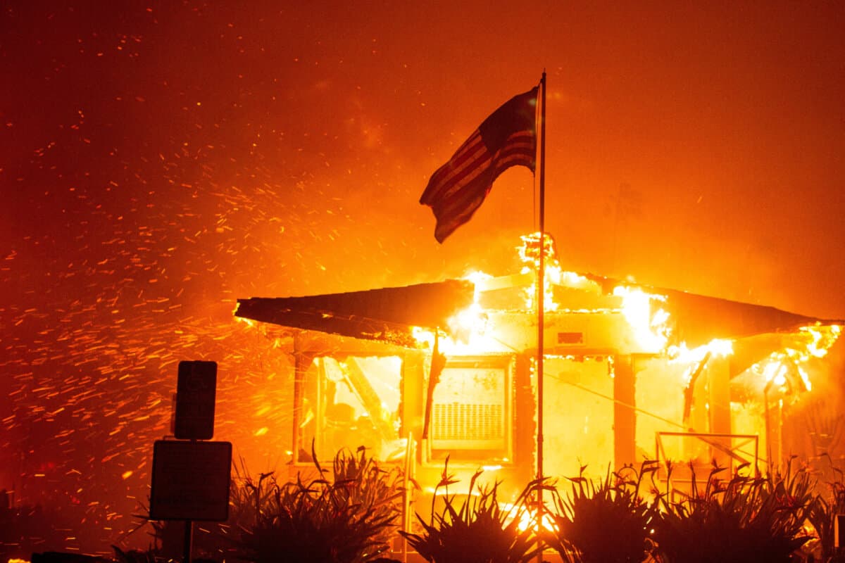 A U.S. flag flies as fire engulfs a structure while the Palisades fire burns during a windstorm on the west side of Los Angeles on Jan. 7, 2025. (Ringo Chiu/Reuters)