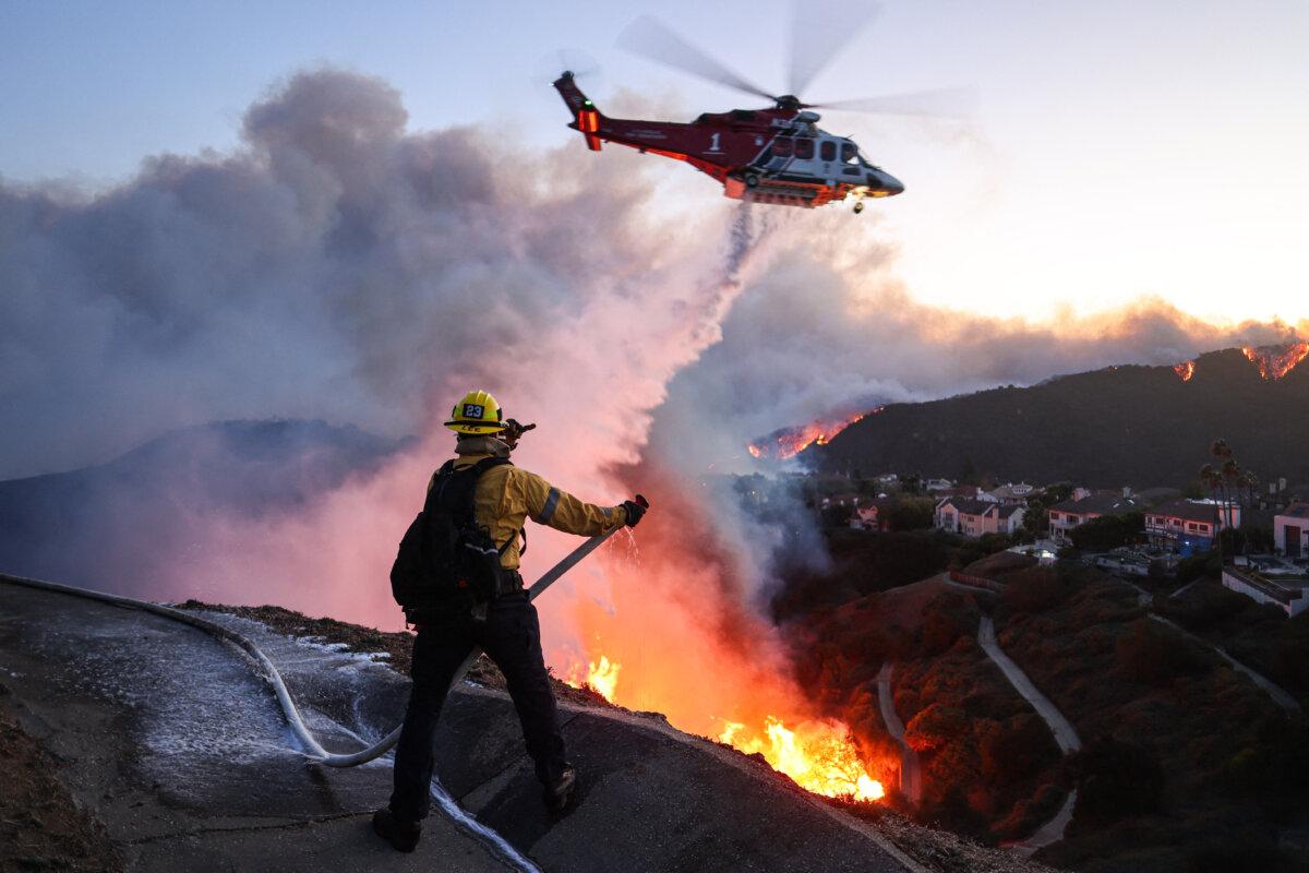 Fire personnel respond to homes destroyed while a helicopter drops water as the Palisades Fire grows in Pacific Palisades, California, on January 7, 2025. (David Swanson/AFP via Getty Images)
