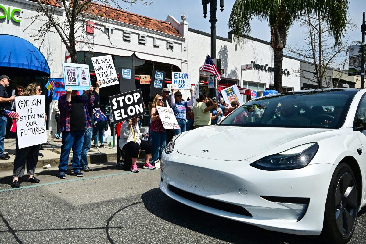 A Tesla car drives past demonstrators rallying against Tesla CEO Elon Musk during a "Tesla Takedown" protest outside a Tesla store in Pasadena, California, on March 29, 2025. (Photo by Frederic J. BROWN / AFP) (Photo by FREDERIC J. BROWN/AFP via Getty Images)