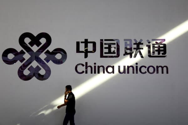A man holding a mobile phone walks past a China Unicom logo during the Mobile World Congress in Shanghai, China, on June 28, 2023. (Nicoco Chan/Reuters)