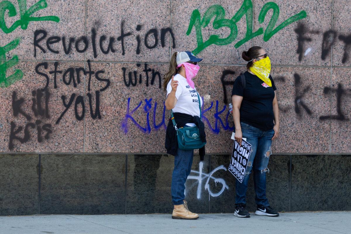 Protesters stand in front of anti-ICE graffiti on a federal building in Los Angeles on June 8, 2025. (John Fredricks/The Epoch Times)