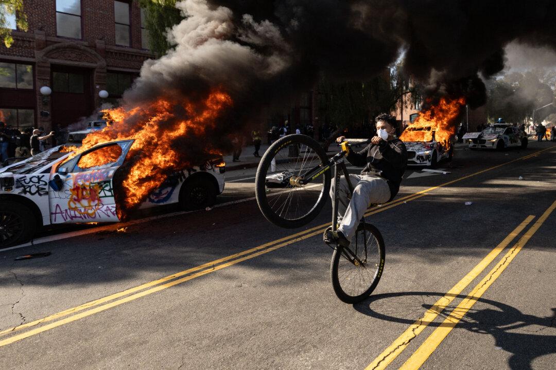 A demonstrator rides a bicycle past burning Waymo vehicles as protesters clash with law enforcement near the federal building during a protest in response to federal immigration operations in Los Angeles on June 8, 2025. (Etienne Laurent/AFP via Getty Images)